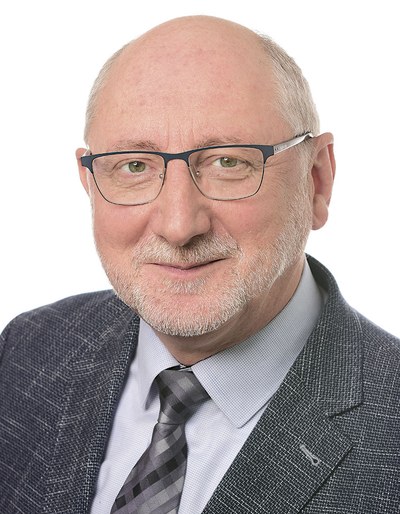 Portraitfoto von Dr. Ronald Unger von der BG ETEM. Er hat eine Halbglatze, trägt eine Brille und einen Anzug.