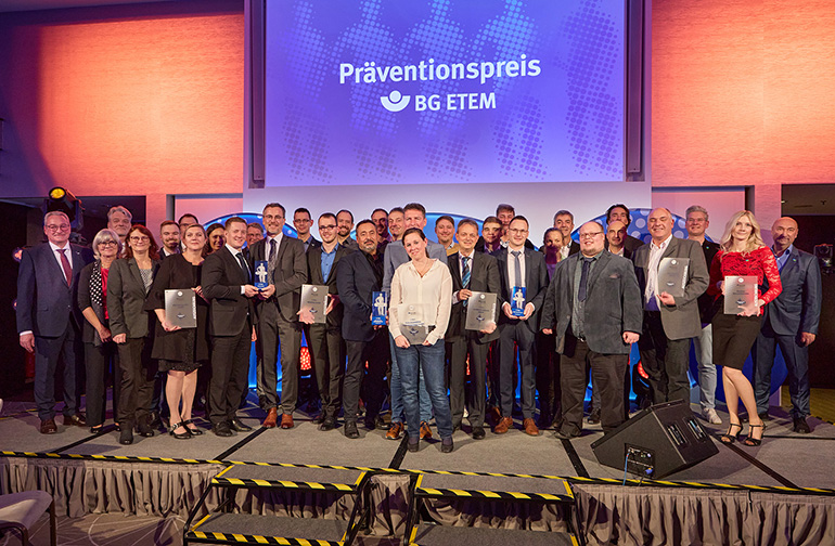 Gruppe von Menschen steht auf einer Bühne, im Hintergrund steht auf einer Leinwand "Präventionspreis BG ETEM".
