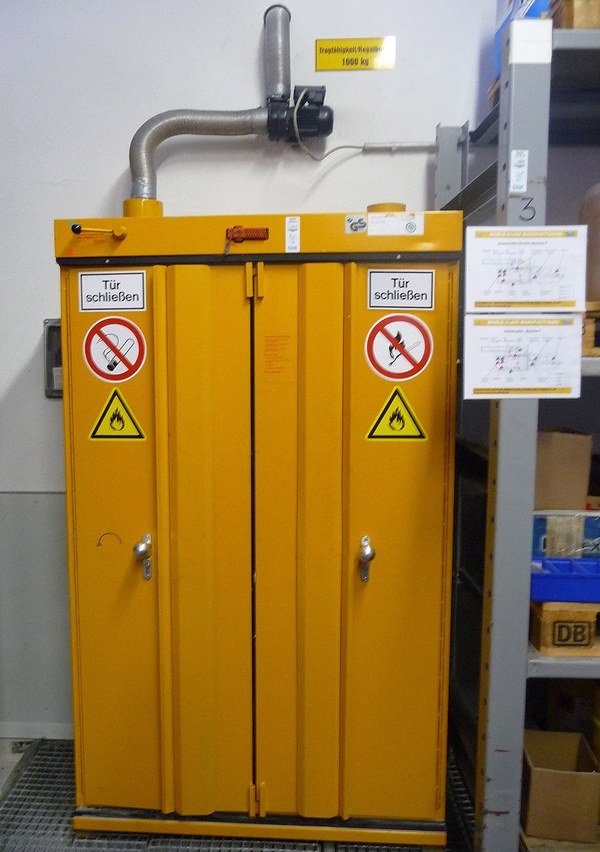 Gefahrstoffschrank: Geschlossener orangener Schrank in Lagerraum.