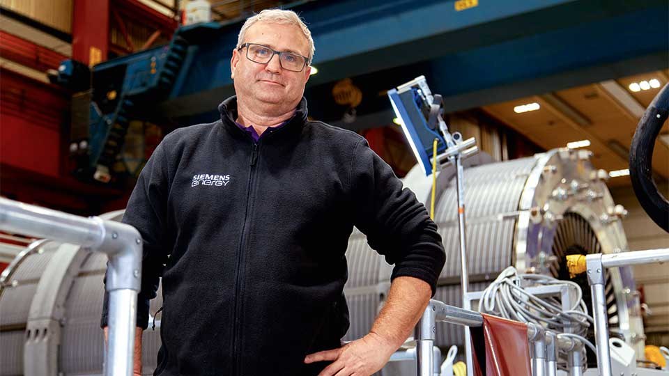 Ein Mitarbeiter von Siemens Energy vor einem großen Elektromotor, der vertikal montiert wurde.