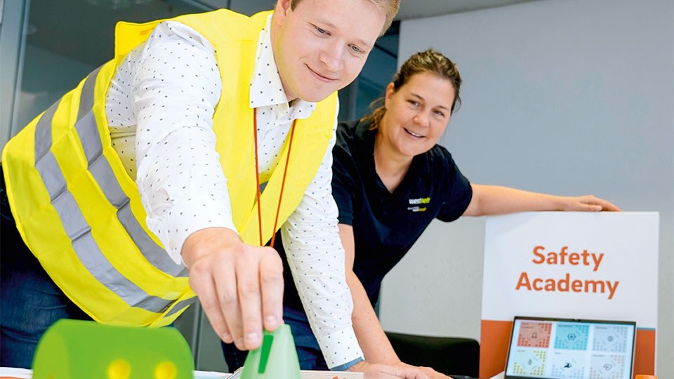 Eine Mitarbeiterin und ein Mitarbeiter  am Spielbrett des interaktiven Wissensspiels Safety Academy.