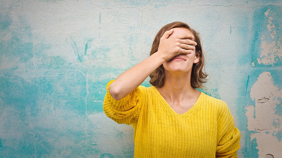 Junge Frau im gelben Pullover schlägt eine Hand vor das Gesicht, weil sie eine Entscheidung bereut, die sie getroffen hat