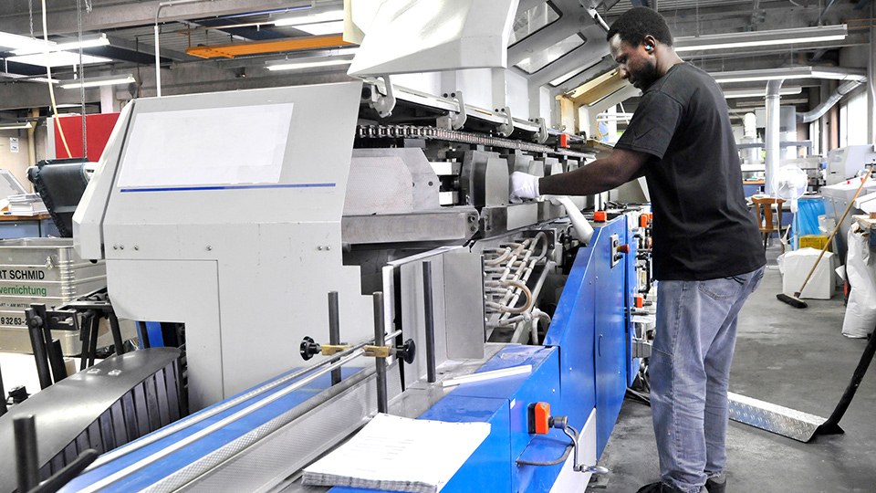 Beschäftigter einer Druckerei an einer Klebemaschine, er trägt Ohrenstöpsel