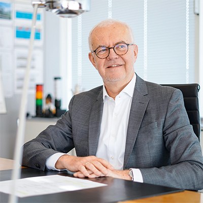 Werma CEO Matthias Marquardt sitzt an seinem Schreibtisch, er blickt in die Ferne; im Vordergrund eine Schreibtischlampe, im Hintergrund ein Whiteboard und an den Wänden ausgedruckte Charts und Pläne.