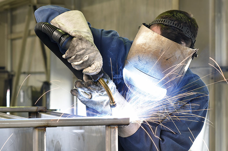 Ein Metallbau-Beschäftigter in Schutzausrüstung schweißt Metallteile zusammen.