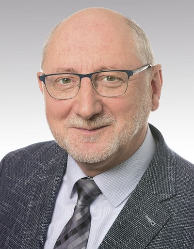 Porträtfoto von Dr. Ronald Unger, Referent der BG ETEM für Sicherheitswerbung, der in die Kamera lächelt. Er hat graue Haare, eine Halbglatze und einen kurzen Vollbart, trägt eine Brille sowie ein graues Jackett mit hellem Hemd und dunkler Krawatte.