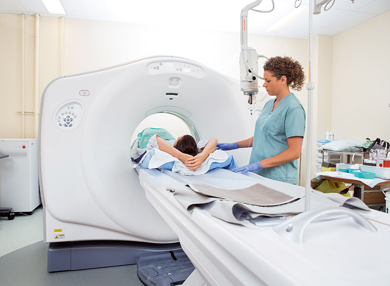 Gesundheitsvorsorge Krebs durch Asbest: Patient auf der Liege eines CT-Gerätes wird von einer Schwester in grüner Klinikkleidung für eine Aufnahme vorbereitet.