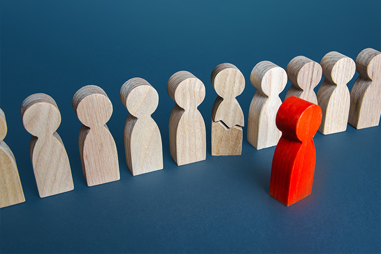 Psychisch auffällige Beschäftigte: Reihe von Spielfiguren aus unlackiertem Holz mit einer zerbrochenen Figur, davor eine rot lackierte Figur.