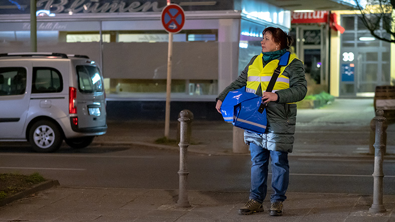 Zeitungszustellerin steht nachts auf einer Straße.