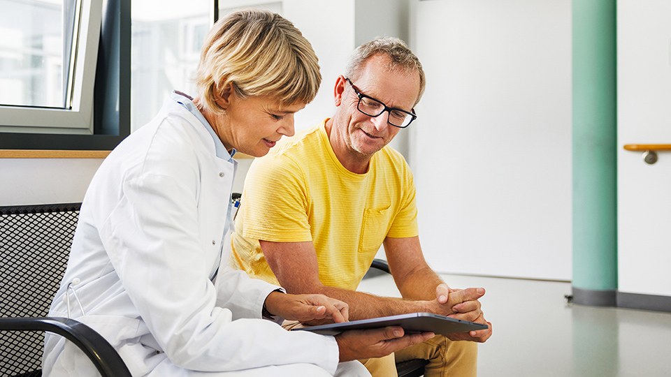 Patient im Gespräch mit einer Ärztin, die einen Tablet-Computer in der Hand hält