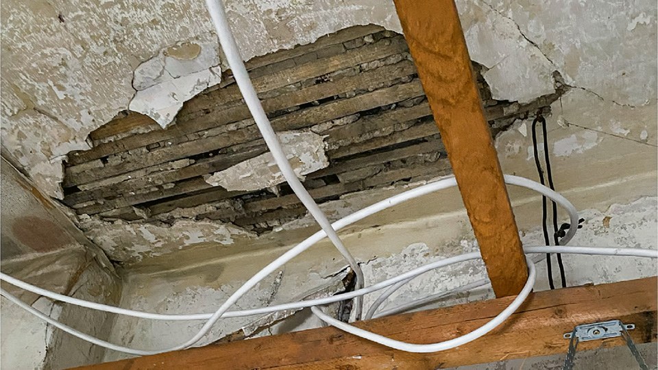 Zwischendecke eines älteren Gebäudes mit teilweise freigelegten Rohren, Kabeln und Holzbalken