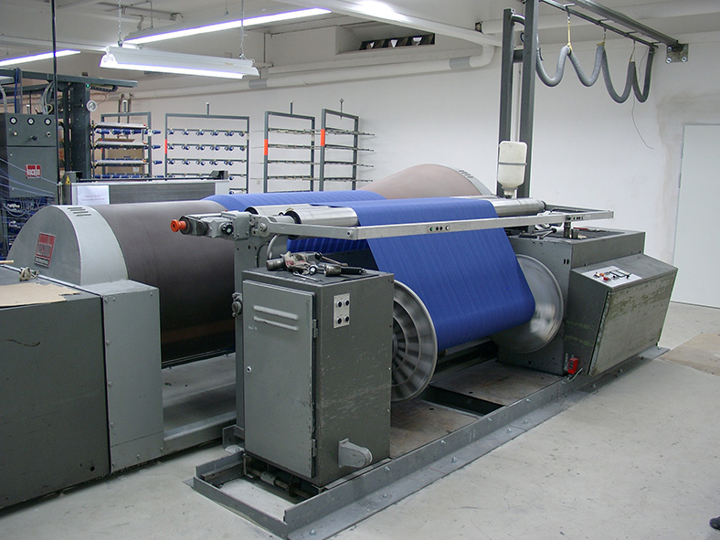 Konusschärmaschine in einer Werkshalle. Die Walzen der Maschine sind mit blauem Stoff umwickelt.