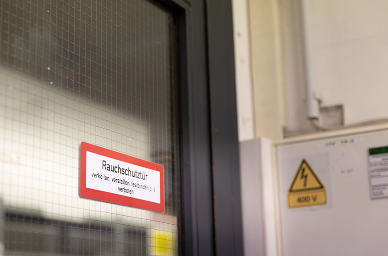 Schild „Rauchschutztür“ auf der Glasscheibe einer Tür.