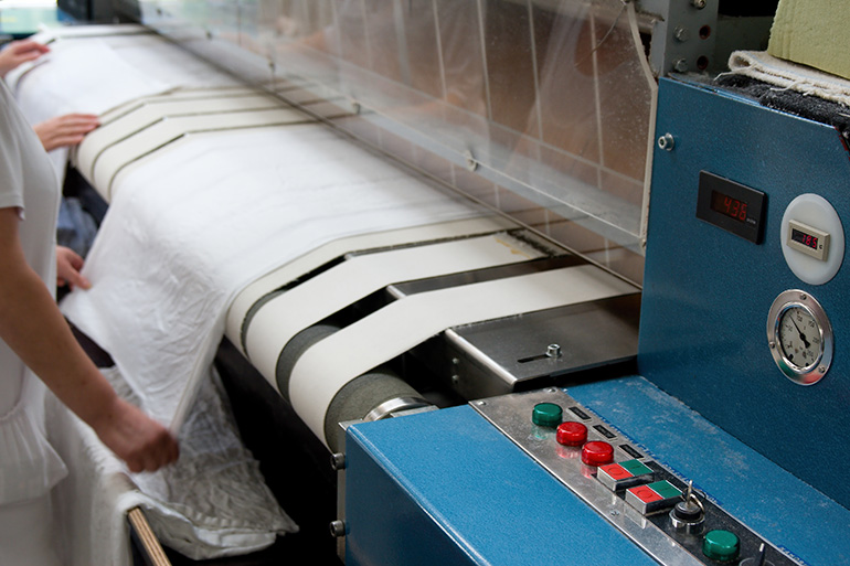 Textilmaschinen: Wäschemangel mit Händen daran arbeitender Frauen.