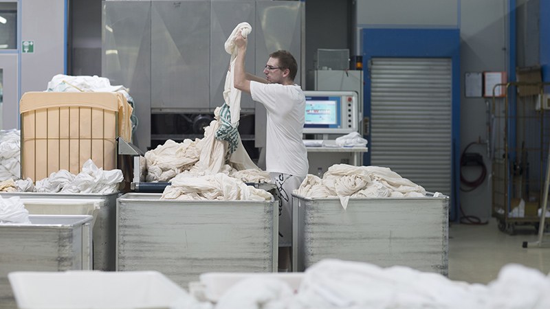 Mitarbeiter einer Wäscherei hebt nasse Bettwäsche aus einem Alu-Kastenwagen