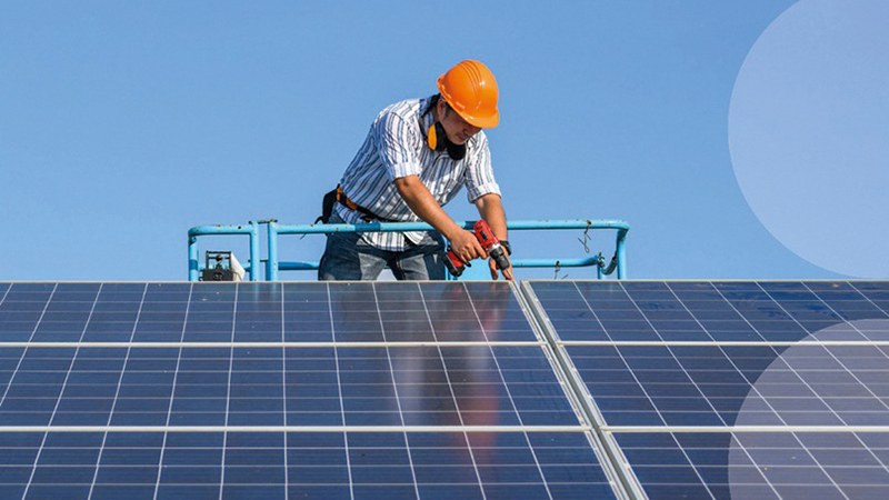 Arbeiter mit Schutzhelm arbeitet an einer Photovoltaikanlage auf einem Dach