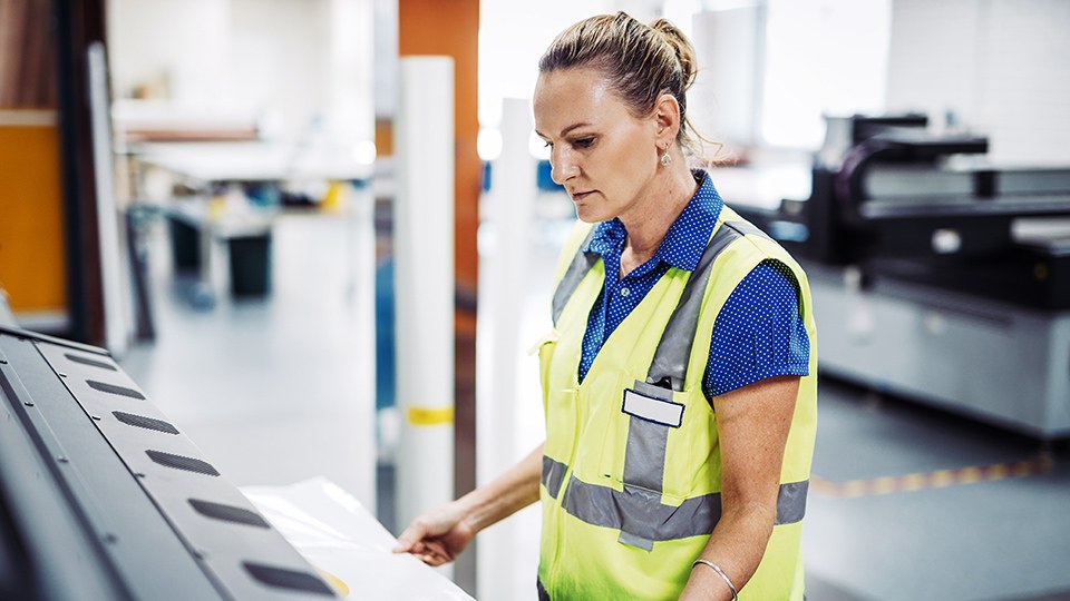 Mitarbeiterin mit Signalweste an einem Bedienpult in einer Druckerei