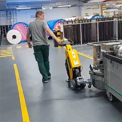 Arbeiter zieht mithilfe einer Rangierhilfe einen schweren Trolley zum Transport von Druckzylinder