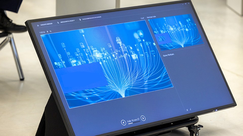 Blick auf Display eines Tablets, auf dem der futuristische blaue Startbildschirm der Präsentation eines Referenten zu sehen ist.