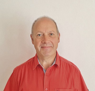 Porträtfoto von Roland Jäschke. Er hat eine Stirnglatze, trägt ein rotes Hemd und lächelt in die Kamera.