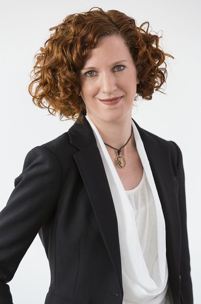 Das Porträtfoto zeigt Kathrin Mohr. Sie trägt lockige halblange Haare, ein dunkles Jackett und ein helles Oberteil.