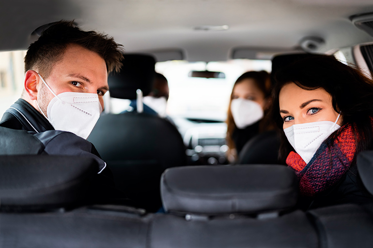 Fahrgemeinschaften: Blick von hinten in den Innenraum eines Pkw. Vier Personen mit FFP2-Masken schauen nach hinten in die Kamera.