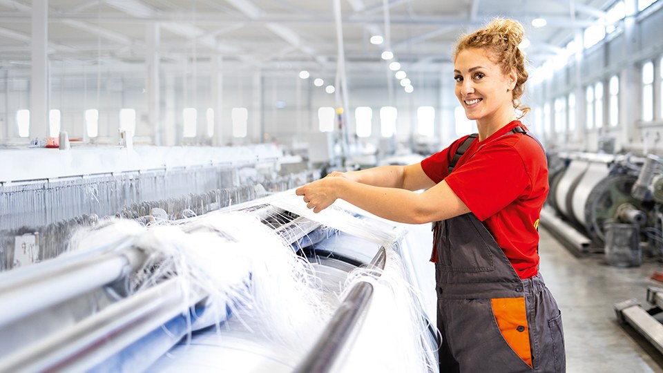 Arbeiterin mit rotem T-Shirt und Arbeitslatzhose in einer Textilfabrik, die Teppiche herstellt.