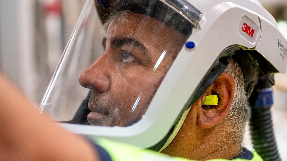Essity-Mitarbeiter Bayram Tarhan an der Maschine, er trägt ein neuartiges Helmsystem mit Vollvisier