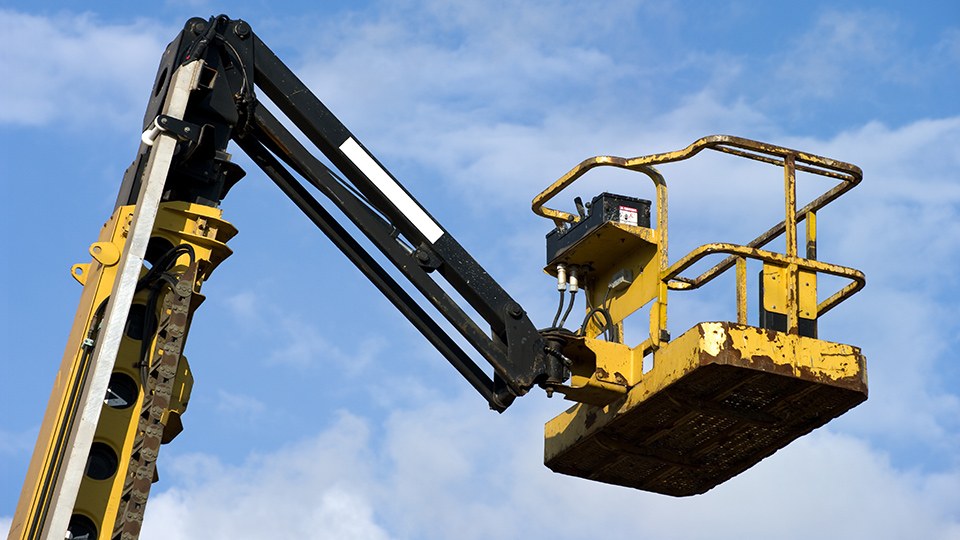Kran mit einer gelben hydraulischen Plattform hoch oben am Himmel