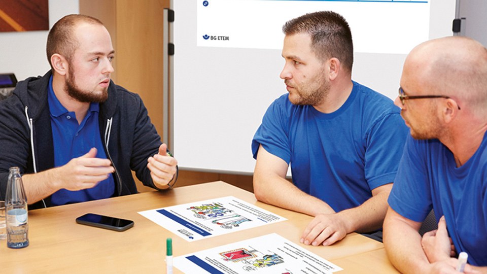Drei Männer an einem Besprechungstisch in einer Schulungs- oder Diskussionssituation