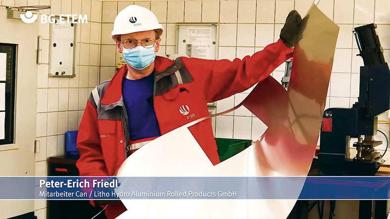 Peter Friedl in Persönlicher Schutzausrüstung mit Helm und Mundschutz hält ein Aluminiummuster mit speziellen, schnittfesten Handschuhen.