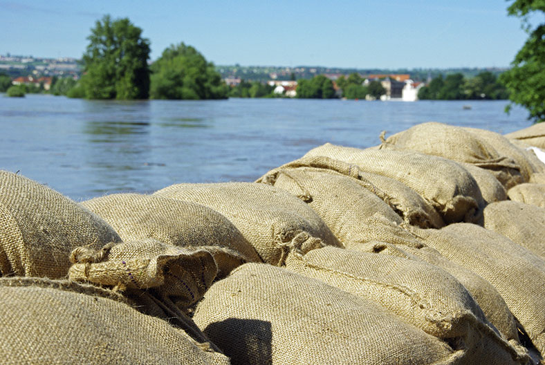 Flutkatastrophe: Sandsäcke an Ufer eines Gewässers.