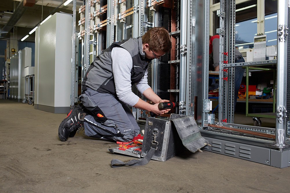 Instandhaltung: Mann mit Werkzeugkoffer arbeitet auf den Knien an elektrischen Anlagen.