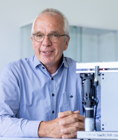 Sicherheitsbeauftragte: Wolfgang Ripken, Chef der Switch-it Assembling GmbH, sitzt mit gefalteten Händen vor einer Lötmaschine. Er hat graue Haare mit einer Stirnglatze, trägt eine Brille und ein blaues Hemd.