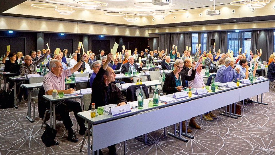 Die Vertreterversammlung bei der Stimmabgabe per Handzeichen in einem großen Saal mit vielen Tischreihen