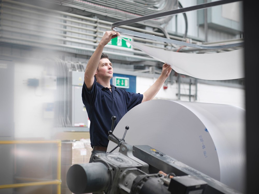 Drucker an der Druckmaschine, im Vordergrund eine Papierrolle