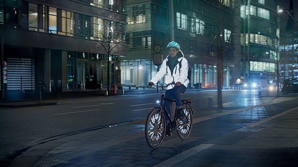 Junger Mann mit hell reflektierender Jacke fährt nachts mit dem Fahrrad auf einer Straße in der Stadt