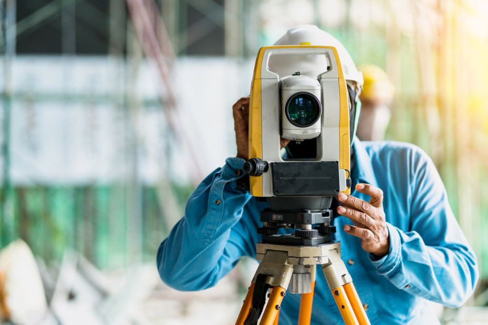 Ingenieur schaut für eine Vermessung durch einen Laser auf einem Stativ, im Hintergrund unscharf eine Baustelle