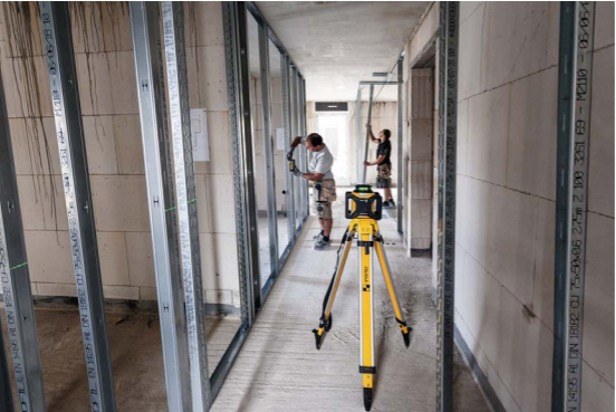 Rotationslaser auf Gang eines im Bau befindlichen Gebäudes, zwei Handwerker beim Trockenbau