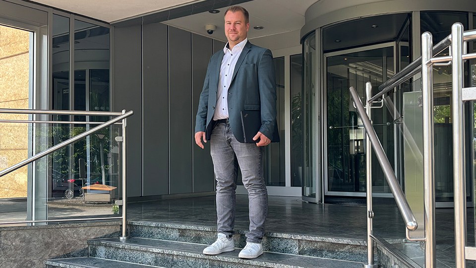 Dennis Wolf geht die Treppe der BG ETEM Hauptverwaltung hinunter, unter dem Arm ein Laptop. Er blickt in die Kamera.