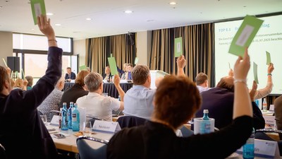 Blick in den Sitzungssaal mit der Vertreterversammlung: Die Teilnehmer stimmen ab, indem sie einen grünen Stimmzettel in die Höhe halten.