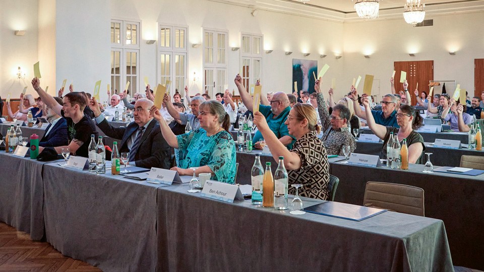 Die Teilnehmerinnen und Teilnehmer der Vertreterversammlung stimmen durch Heben des Stimmzettels ab