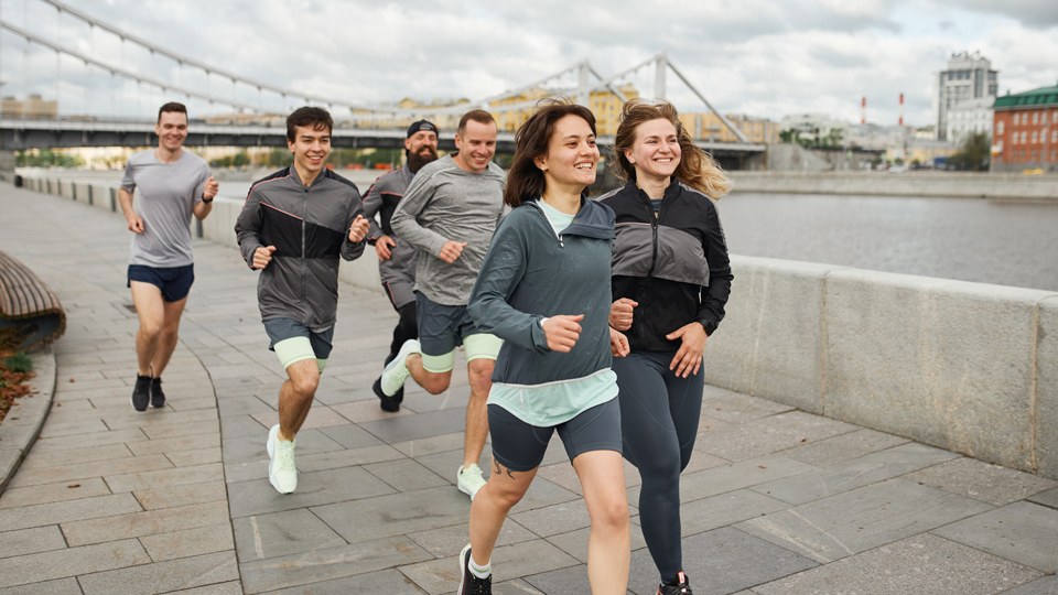 Laufgruppe aus 6 jungen Erwachsenen an einer Flusspromenade