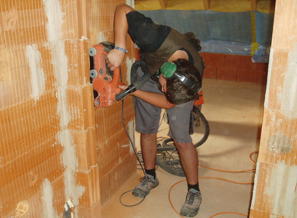 Handwerker arbeitet gebückt mit einer Schlitzfräse an einer Innenwand.