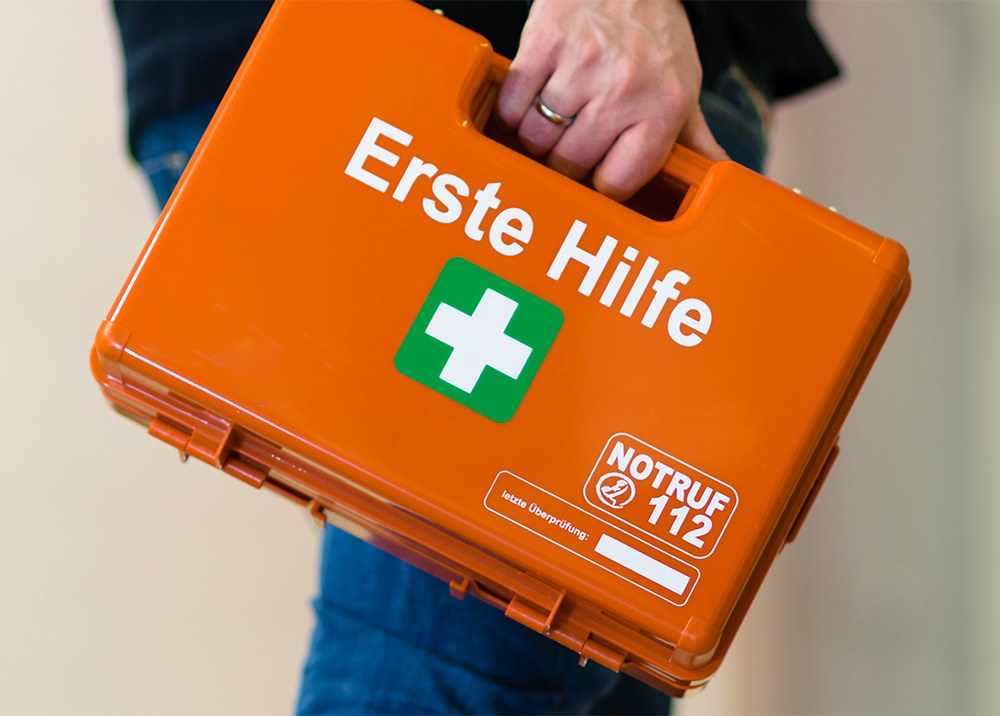 Arbeitsunfall: Mann trägt orangenen Erste-Hilfe-Koffer.