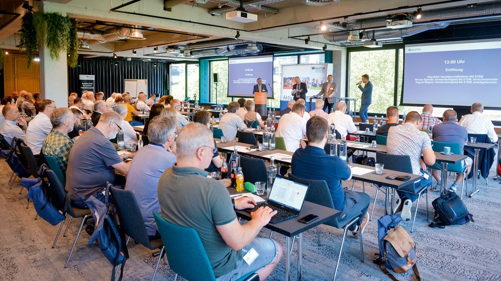 Blick aus den hinteren Reihen einer Tagung auf eine Podiumsdiskussion.