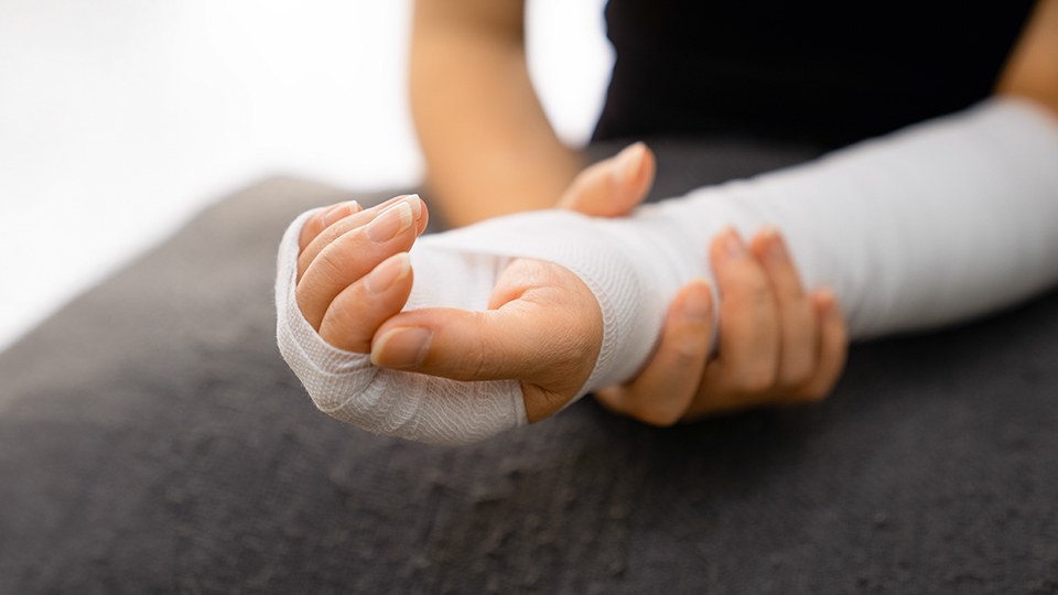 Die linke Hand und der Unterarm sind einbandagiert, die rechte Hand hält das linke Handgelenk und unterstützt.