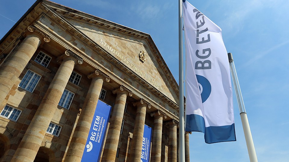 Front der Stadthalle Kassel, davor an einem Mast eine Fahne der BG ETEM.